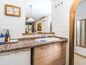 Une salle de bain dotée d’un comptoir en granit, d’un lavabo, d’un meuble en bois, d’un miroir, d’une horloge et d’un élément décoratif mural.