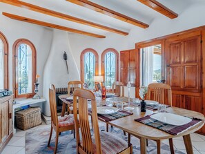 A dining area with wooden furniture, a table set for four, and a view through arched windows. - El Refugio de Rembrandt by Interhome (Jávea)