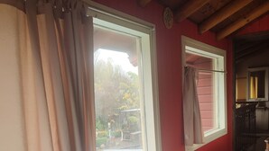 Quarto com cama, janela com cortinas, teto de madeira e vista para o exterior.