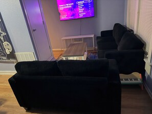 Ein Wohnzimmer mit einer schwarzen Couch, einem kleinen Tisch und einem an der Wand befestigten Fernseher, der einen WLAN-Netzwerkbildschirm anzeigt.