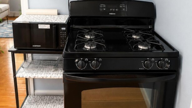 A compact kitchen with a black stove, a microwave, and a small shelf with pots. - Cowboys Field Stay Near River Walk & Alamo (San Antonio)