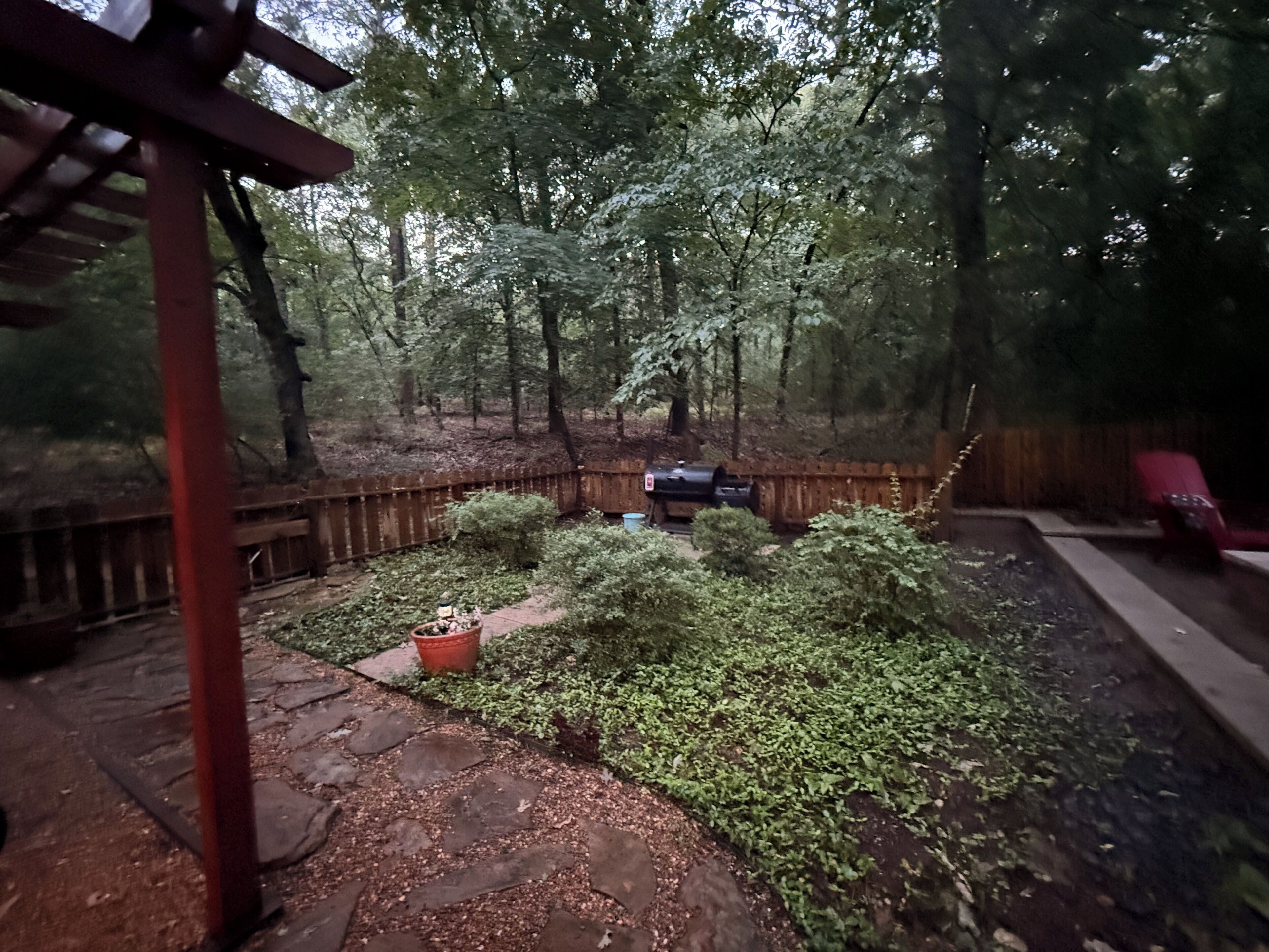 A backyard with a wooden deck, a barbecue grill, and a red chair.