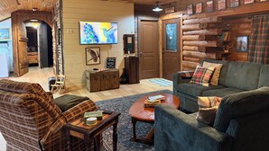 L’intérieur d’un chalet confortable, avec un plafond en bois, un téléviseur, une cheminée et un canapé.