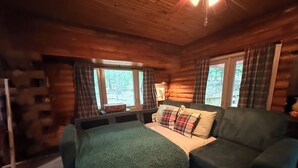 Une chambre de style rustique, avec un lit, un canapé, des rideaux à carreaux et une fenêtre donnant sur la forêt.