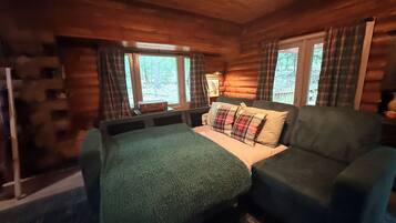 A log cabin room with a bed, a sofa, plaid curtains, and a window with a view of trees.