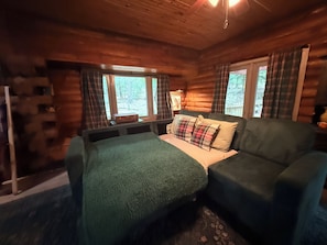 Une chambre de style rustique, avec un lit, un canapé, des rideaux à carreaux et une fenêtre donnant sur la forêt.