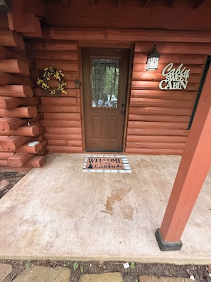 L’entrée d’un chalet en bois, avec une porte, un paillasson et une pancarte sur laquelle on peut lire : « Chalet, mon doux chalet ».