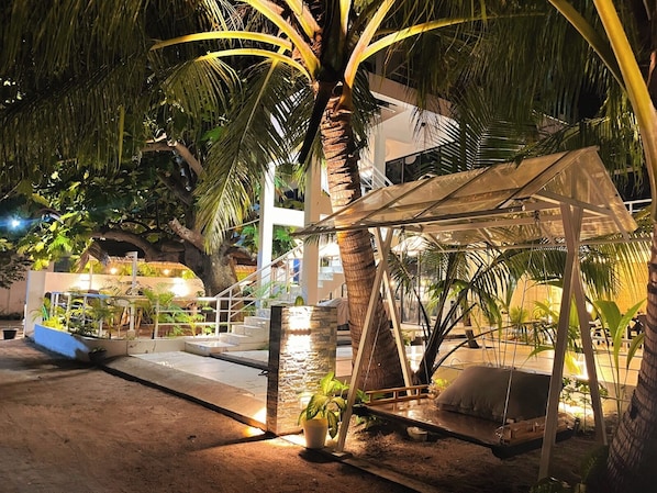 Un espacio exterior bien iluminado con una palmera, una zona de estar cubierta y un muro de piedra.
