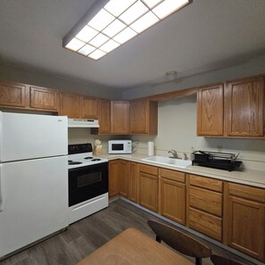 A kitchen with wooden cabinets, a white refrigerator, a stove, a microwave, and a sink.