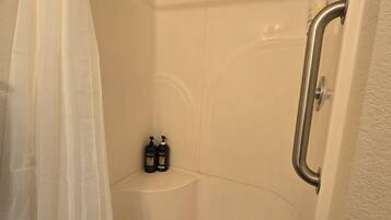 A shower stall with a white curtain, a handheld showerhead, and two bottles of shampoo.