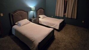 Quarto com duas camas, mesa de cabeceira com abajur, janela com cortinas e luminária no teto.
