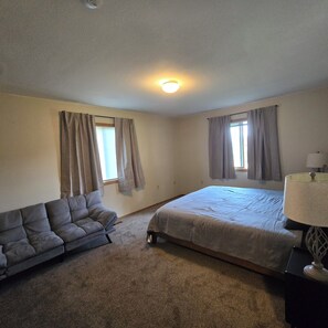 A bedroom with a bed, a sofa, a lamp, and two windows with curtains.
