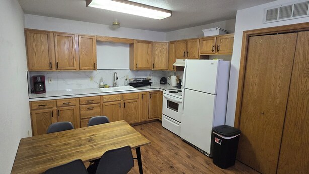 A compact kitchen with wooden cabinets, a refrigerator, a stove, and a dining table with chairs.