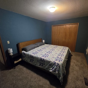 A bedroom with a bed, a nightstand, a lamp, a wooden door, and a ceiling light.