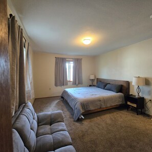 A bedroom with a bed, two bedside tables, a window with curtains, a ceiling light, and a sofa. - Serene 2-bedroom house with AC and garage in charming Potter. (Potter)