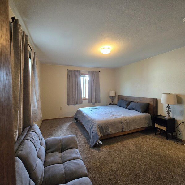 A bedroom with a bed, two bedside tables, a window with curtains, a ceiling light, and a sofa.