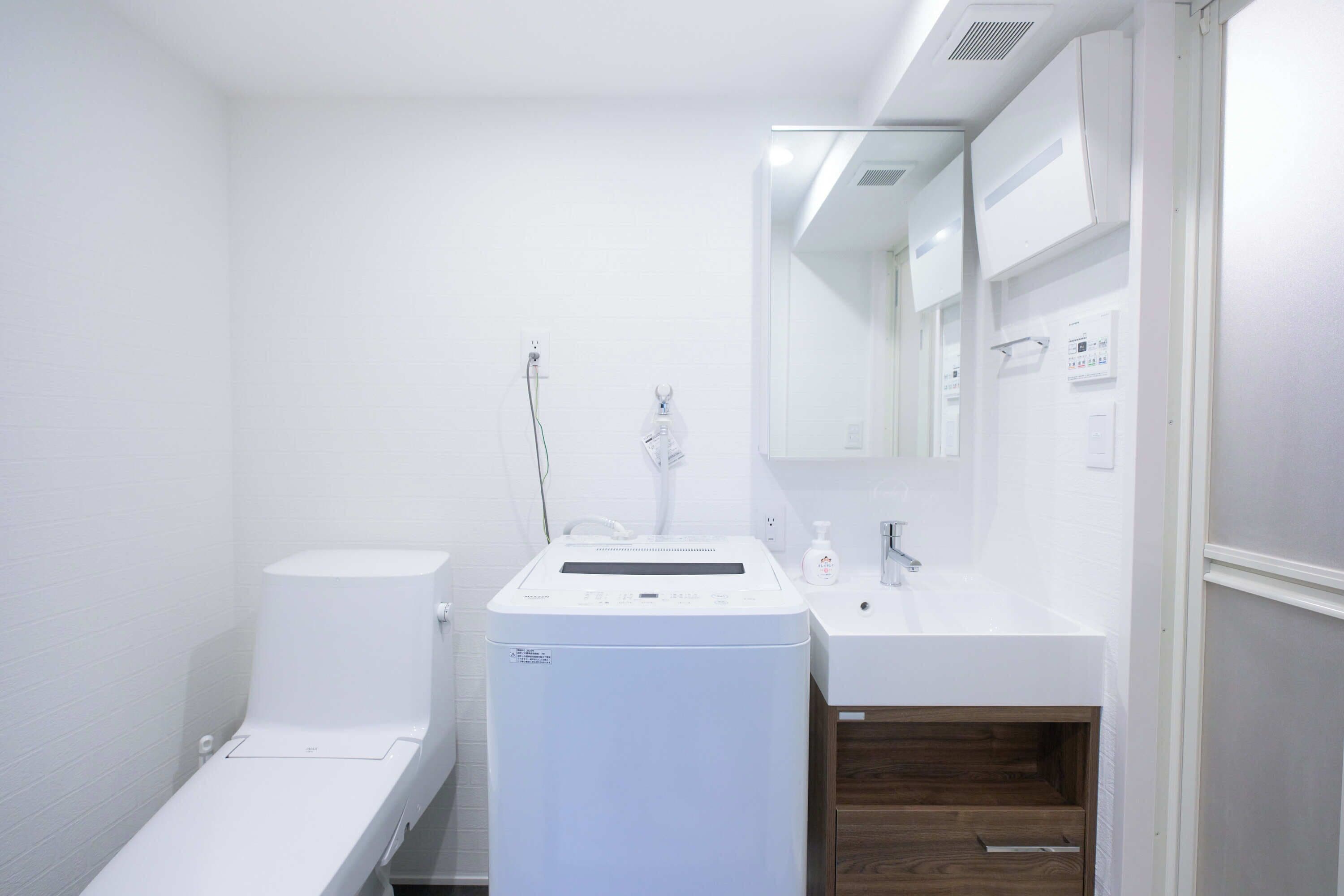 Ein kleines Badezimmer mit Toilette, Waschmaschine, Waschbecken und Spiegel.