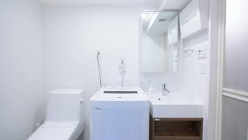 Ein kleines Badezimmer mit Toilette, Waschmaschine, Waschbecken und Spiegel.