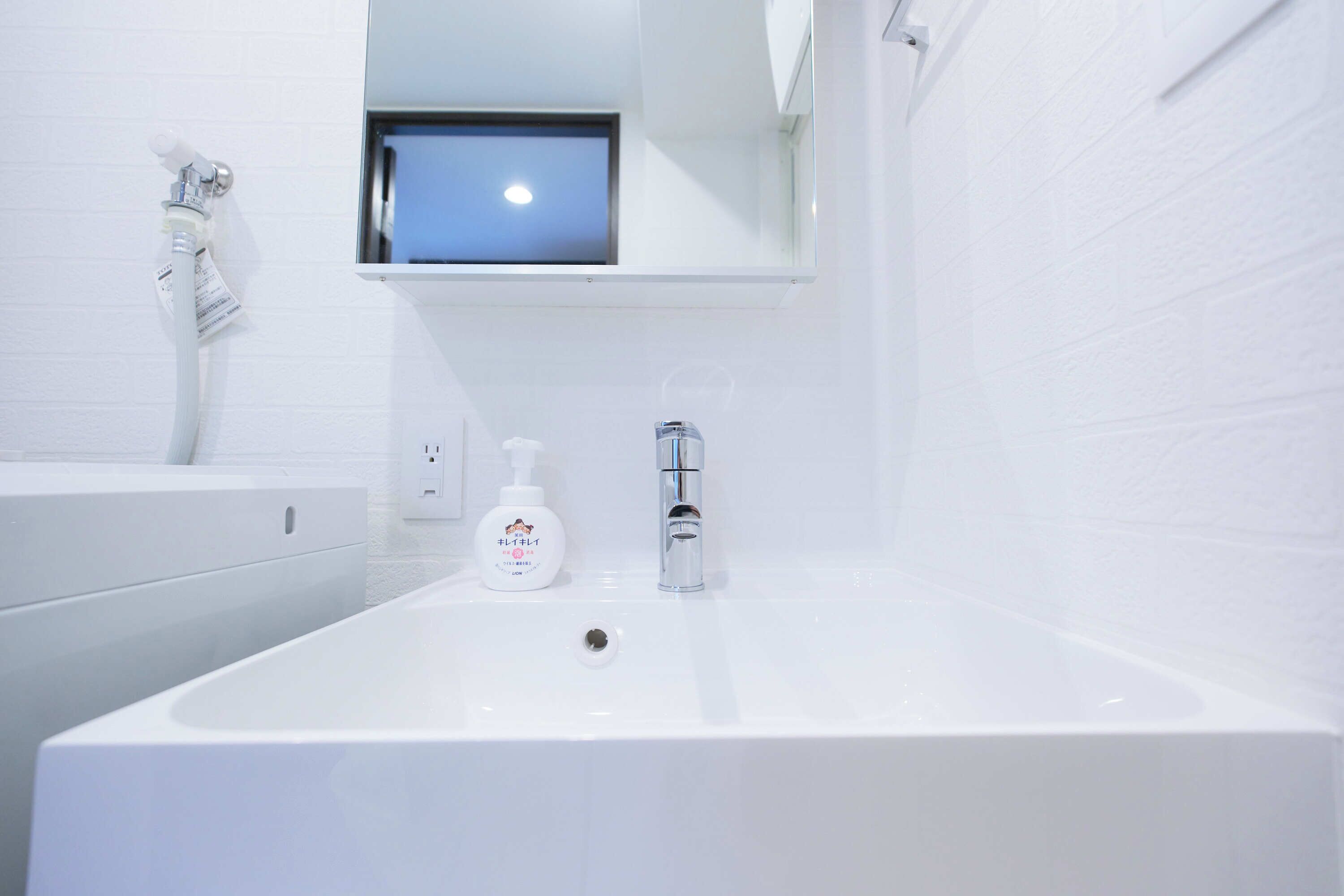 A modern bathroom with a large white sink, a handheld showerhead, and a small window above the mirror.