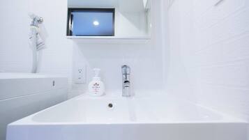 A modern bathroom with a large white sink, a handheld showerhead, and a small window above the mirror.