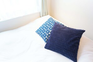 A bed with white bedding and two pillows, one with a geometric pattern and the other knitted. - Bellie Sangenjaya by Tranova 2 (Setagaya City)