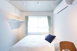 Habitación de hotel con cama, una silla, ventana con cortinas, equipo de aire acondicionado e iluminación en el techo.