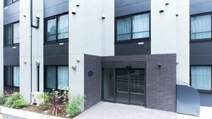 A modern building with multiple windows, a door with glass panels, and a small garden area with plants. - Bellie Sangenjaya by Tranova 2 (Setagaya City)