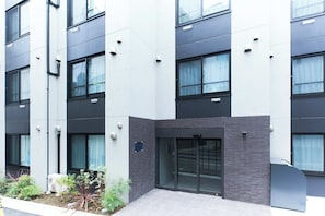Un edificio moderno con varias ventanas, una puerta con paneles de vidrio y un pequeño jardín con plantas.