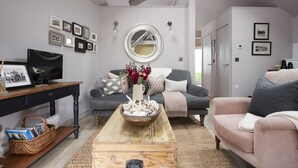 Un salon avec un canapé gris, une table basse en bois et un fauteuil gris. On y trouve des tableaux encadrés au mur, un miroir et une petite table avec un panier.