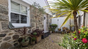 Un bâtiment en pierre doté d’une fenêtre, de plantes en pot et d’un chemin recouvert de gravier.