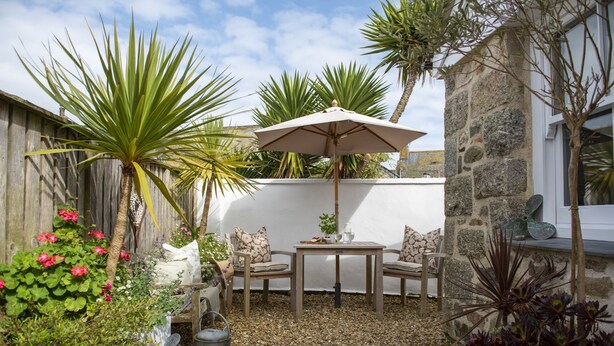 Une terrasse avec une table et des chaises, entourée de plantes et d’un mur en pierre.