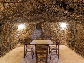 An underground dining area with a table and chairs, surrounded by rough rock walls. - Villa La Grotta by Interhome (Acquapendente)
