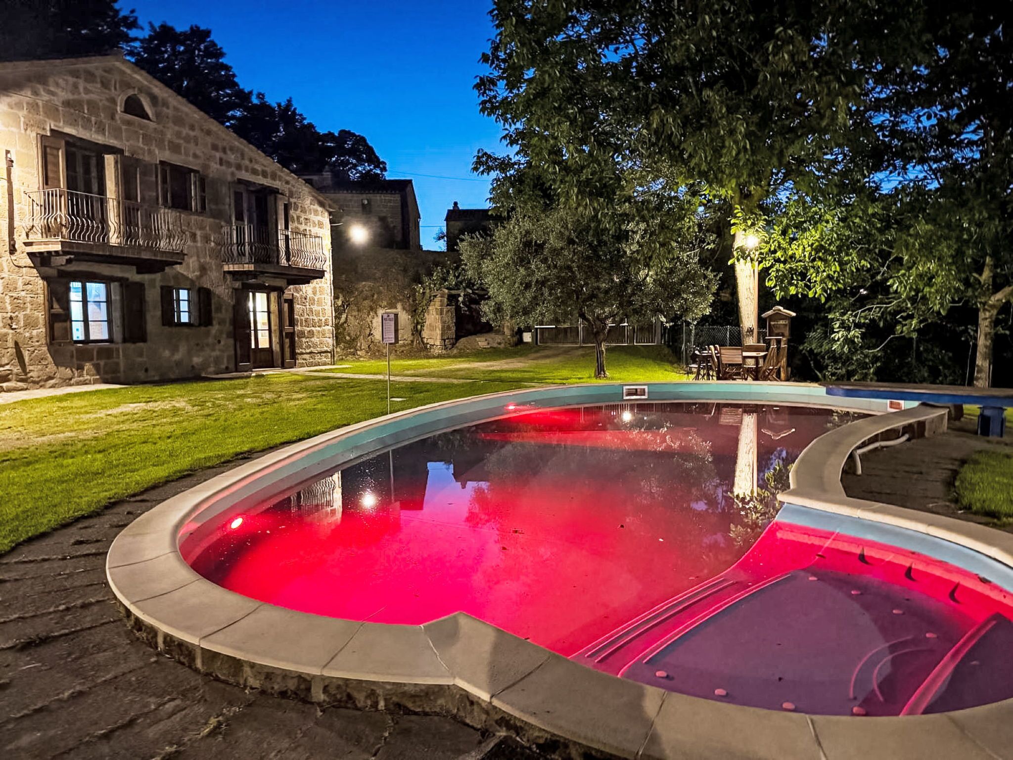 Une piscine au design incurvé, entourée d’un bâtiment en pierre doté d’un balcon et d’une pelouse.