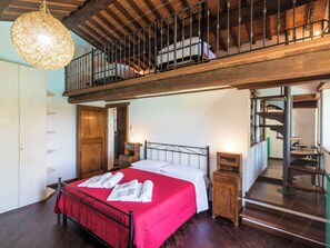 Un dormitorio con una cama, una colcha roja, un armario de madera, una lámpara colgante y una escalera que conduce a un nivel superior.