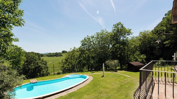 A swimming pool surrounded by a grassy lawn, trees, and a wooden deck with a railing. - Villa La Grotta by Interhome (Acquapendente)