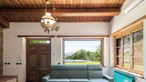 A room with a wooden ceiling, a green sofa, a round table, and a view of a pool and landscape through large windows. - Villa La Grotta by Interhome (Acquapendente)