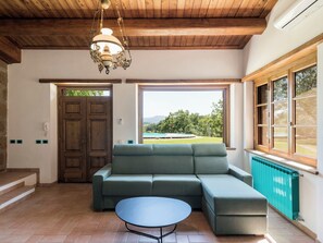 Ein Zimmer mit Holzboden, einem grünen Sofa, einem runden Tisch und Blick auf einen Pool und die Landschaft durch große Fenster.