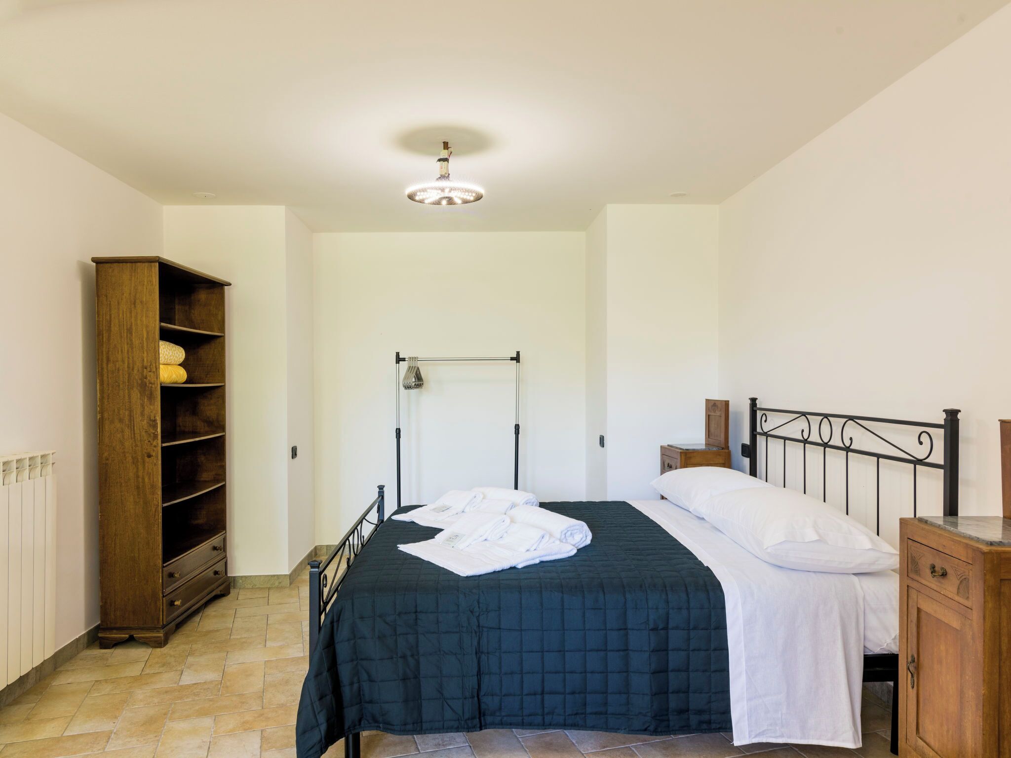 Une chambre à coucher comprenant un lit, une armoire en bois, un radiateur et un luminaire fixé au plafond.