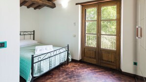 A bedroom with a bed, wooden ceiling beams, a window with a view of trees, and a wardrobe. - Villa La Grotta by Interhome (Acquapendente)