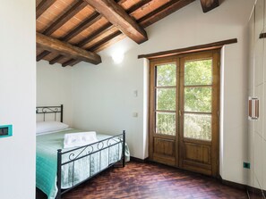 Ein Schlafzimmer mit Bett, Holzbalkendecke, einem Fenster mit Blick auf Bäume und einem Kleiderschrank.