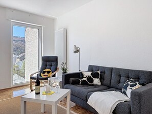 A living room with a grey sofa, a chair, a table with a bottle and glasses, a floor lamp, and a view through a door. - Cozy Home Lahnstein by Interhome (Lahnstein (Koblenz))