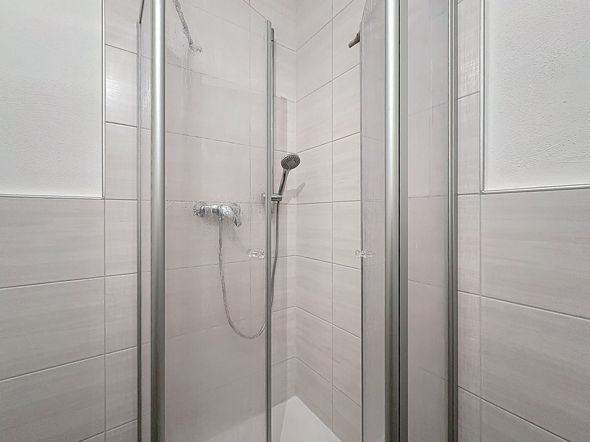 A glass-enclosed shower stall with a handheld showerhead and a wall-mounted faucet.