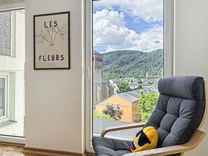A room with a large window, a framed picture of flowers, and a grey armchair with a cushion. - Cozy Home Lahnstein by Interhome (Lahnstein (Koblenz))