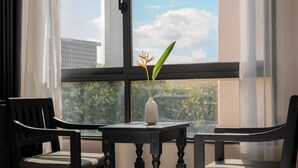 A hotel room with a large window, a round table with two chairs, and a vase with a plant. - Jolia Nha Trang Hotel (Nha Trang)