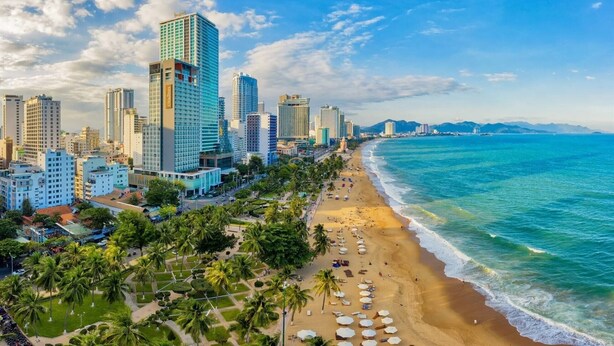 A coastal cityscape with high-rise buildings, a sandy beach, and palm trees. - Jolia Nha Trang Hotel (Nha Trang)