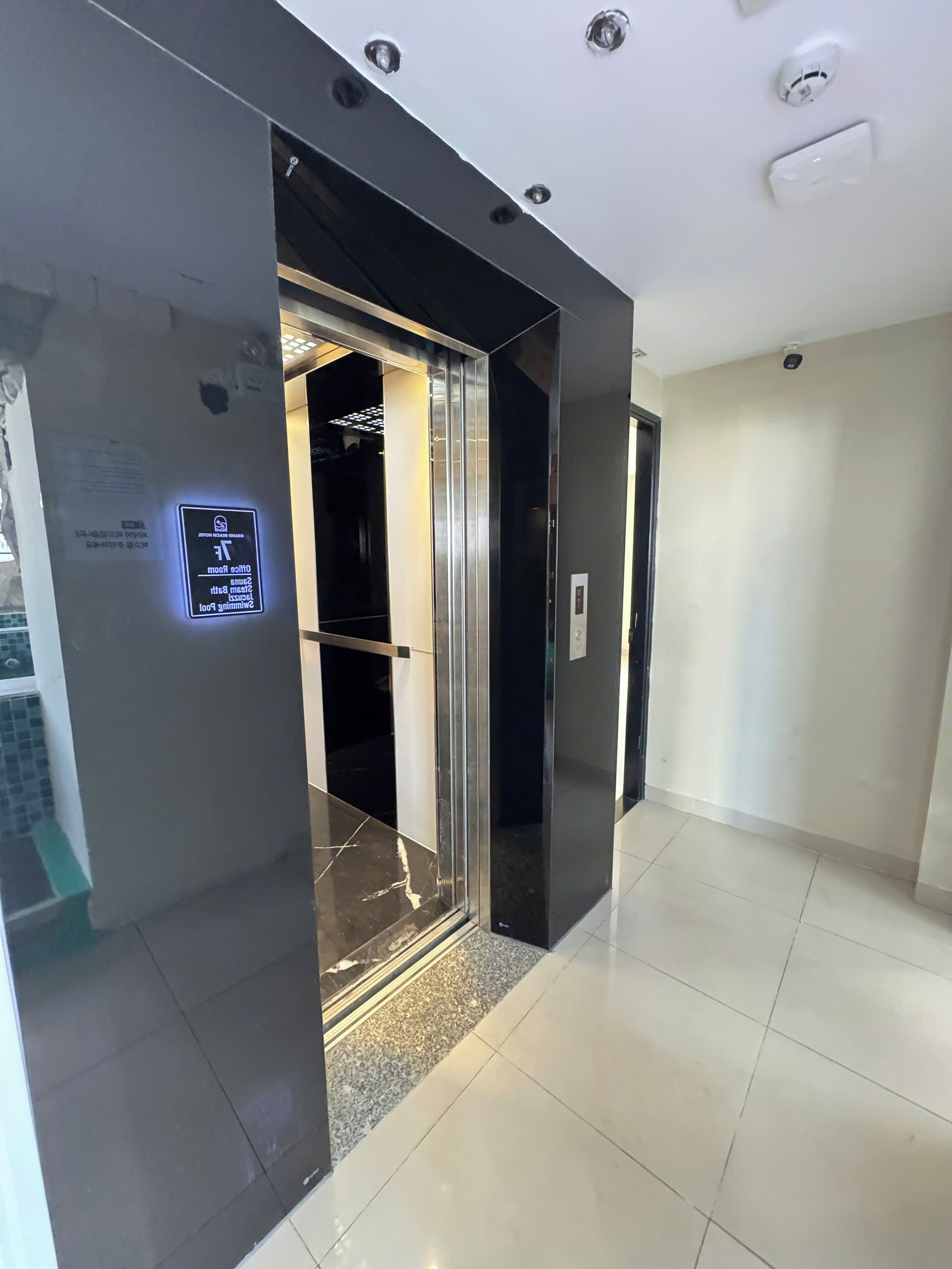 A modern elevator with a digital display, a tiled floor, and a plain wall.