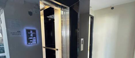 A modern elevator with a digital display, a tiled floor, and a plain wall.
