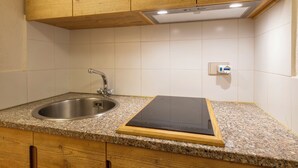 Eine Küche mit Granit-Arbeitsplatte, Spüle aus Edelstahl, Holzschränken und einem schwarzen Induktionskochfeld.