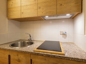 Eine Küche mit Granit-Arbeitsplatte, Spüle aus Edelstahl, Holzschränken und einem schwarzen Induktionskochfeld.