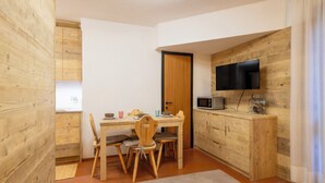 Eine kleine Küche mit Holzausstattung, einem Esstisch mit Stühlen, einer Mikrowelle und einem an der Wand befestigten Fernseher.